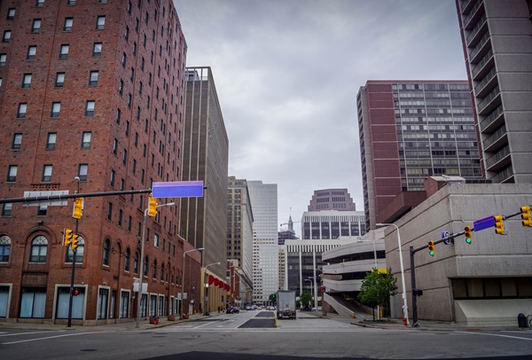 Downtown Cleveland street lined with tall buildings and traffic signals on a cloudy day, with minimal vehicle and pedestrian activity.