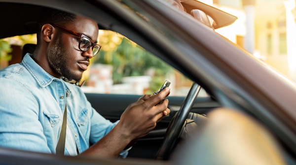 Driver using a smartphone while seated behind the steering wheel of a passenger vehicle, depicting distracted driving and potential crash liability